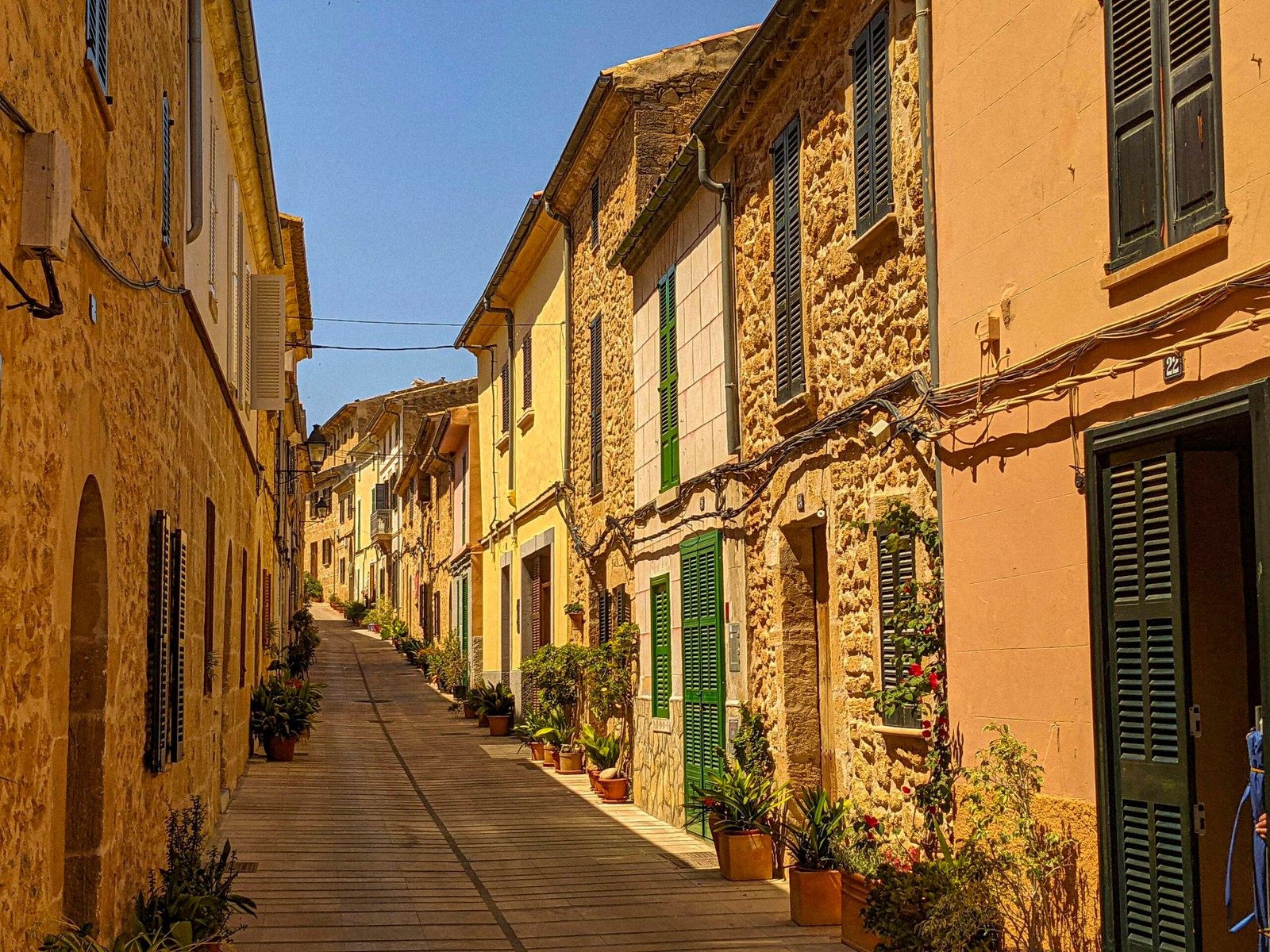 Enge Straße auf Mallorca mit alten Steinbauten und grünen Fensterläden, fotografiert von Andre Blanco