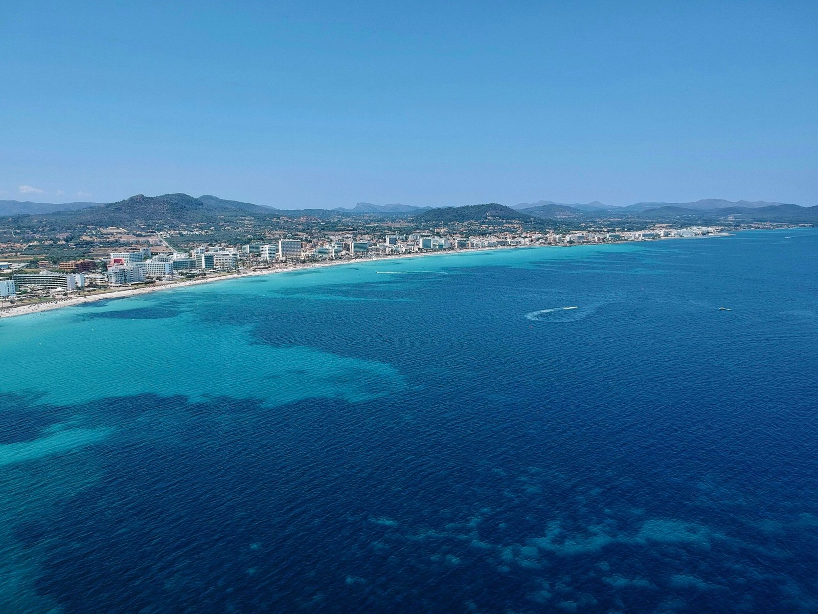 Stadt auf dem Wasser auf Mallorca mit Gebäuden am Ufer und einem ruhigen Wasser spiegelnd, aufgenommen von Leon Rohrwild.