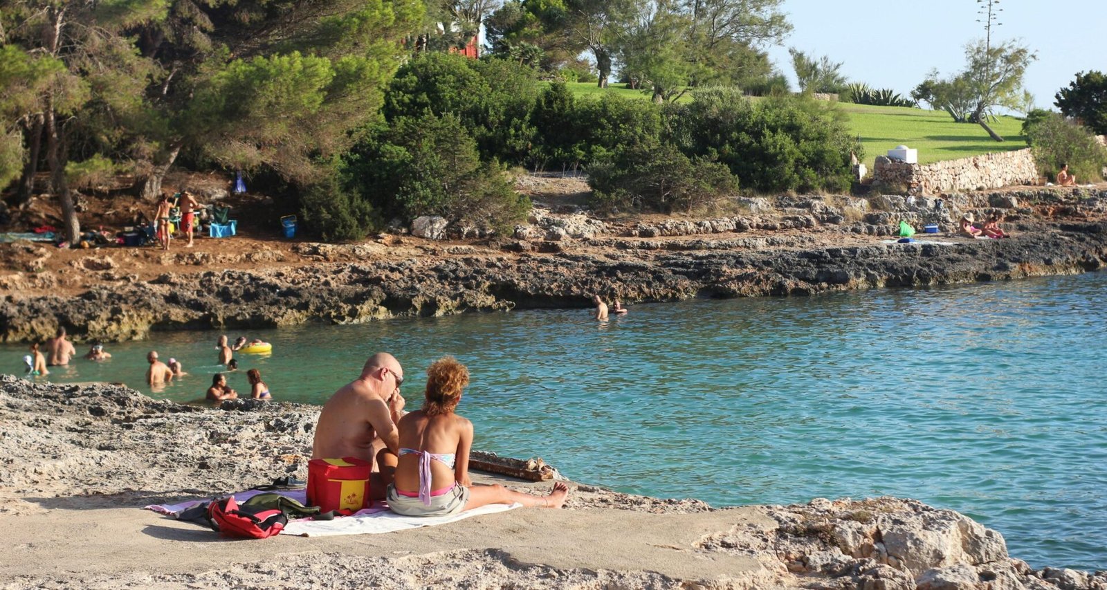 Frau in pinkem Bikini liegt entspannt auf Sand am Strand auf Mallorca bei Tageslicht, Blick auf das Wasser