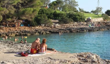 Frau in pinkem Bikini liegt entspannt auf Sand am Strand auf Mallorca bei Tageslicht, Blick auf das Wasser