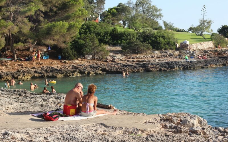 Frau in pinkem Bikini liegt entspannt auf Sand am Strand auf Mallorca bei Tageslicht, Blick auf das Wasser