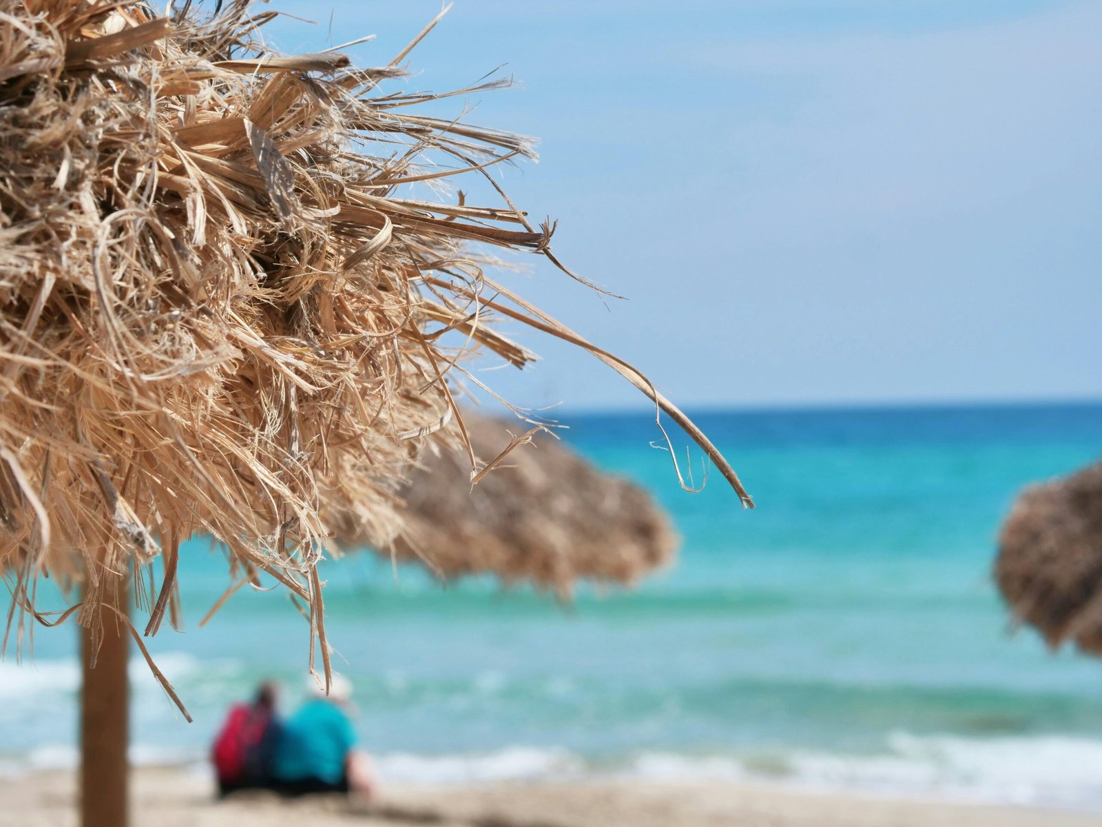 Frau in rotem Shirt steht während des Tages am Strand auf Mallorca, Blick auf das Meer