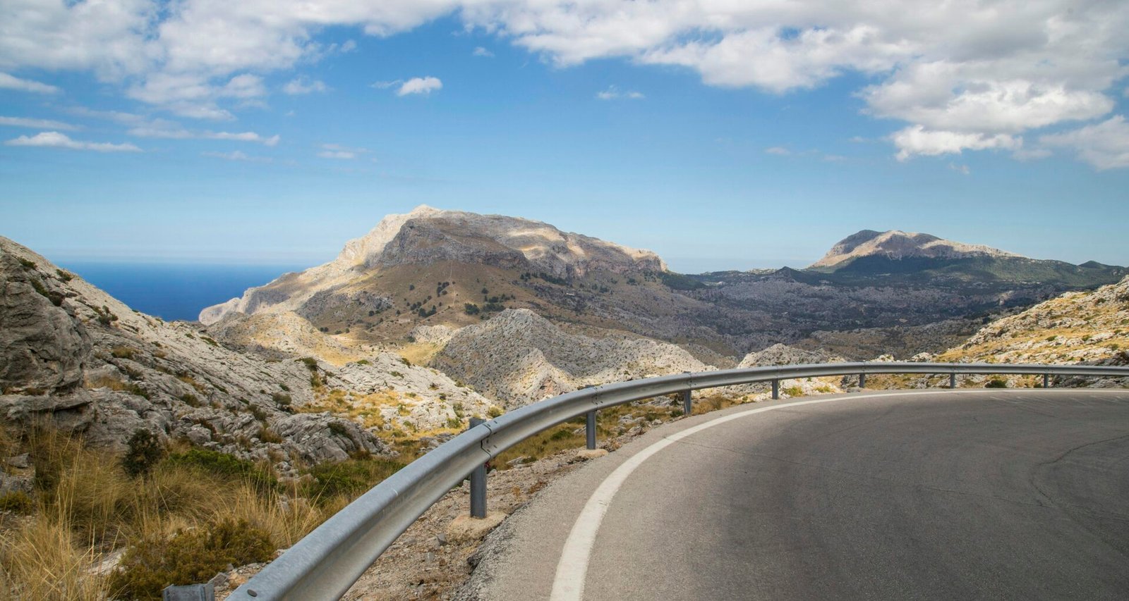 Graue Betonstraße auf Mallorca neben braunen Bergen unter blauem Himmel, aufgenommen bei Tageslicht von Milada Vigerova