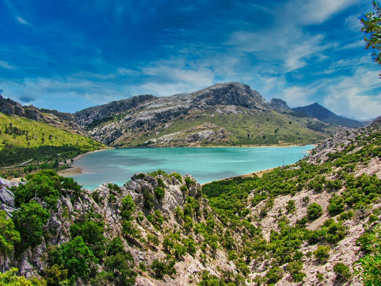 Grüne und braune Berge neben einem Wasser auf Mallorca unter blauem Himmel bei Tageslicht, aufgenommen von DJ Nick Otronic