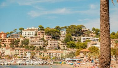 Küstenstadt auf Mallorca mit Gebäuden auf einem Hügel, Blick auf den Strand im Vordergrund, aufgenommen von Alexis Presa.