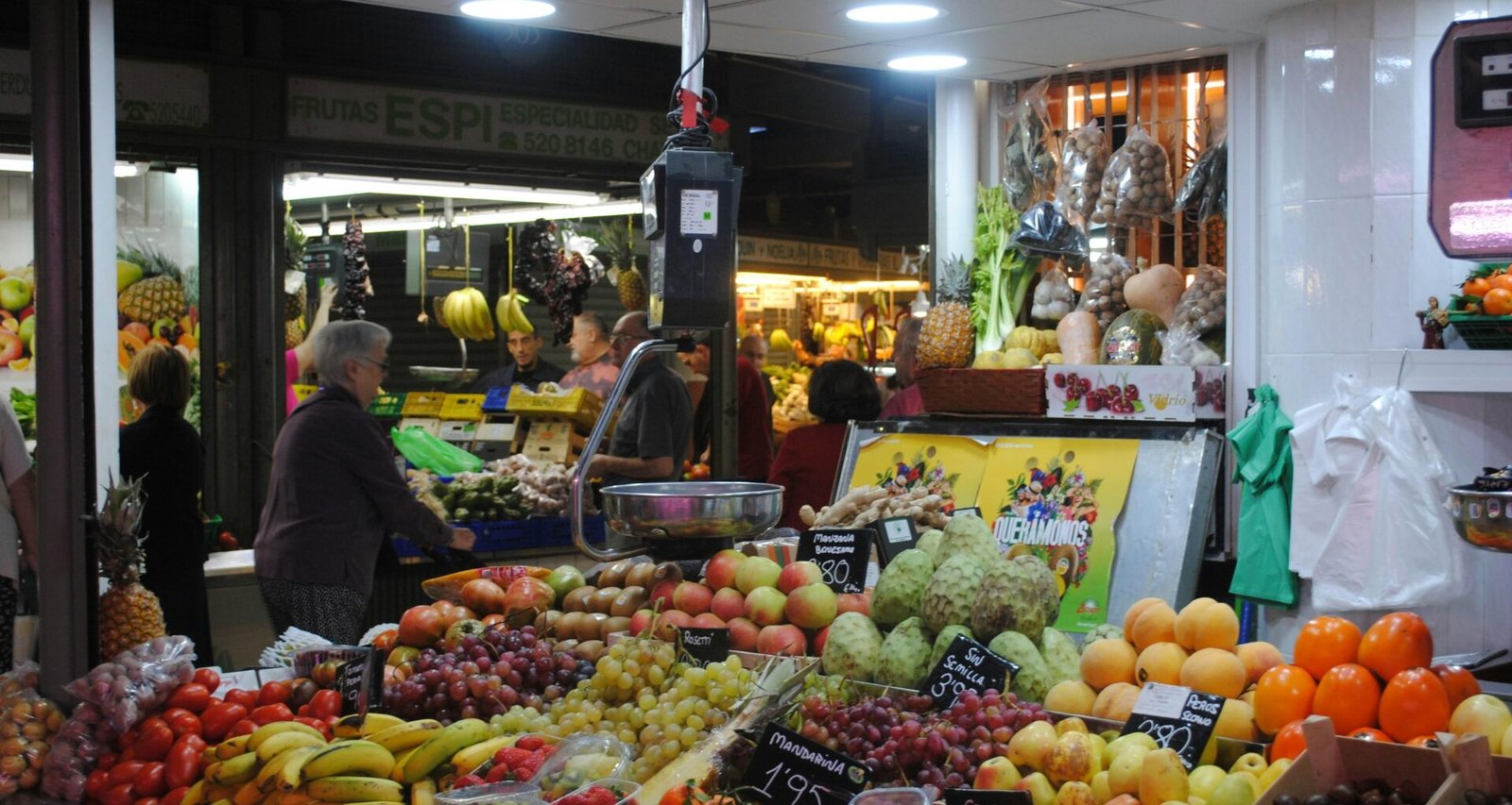 Mann in grauer Jacke steht neben Obststand auf Mallorca, umgeben von frischen Früchten