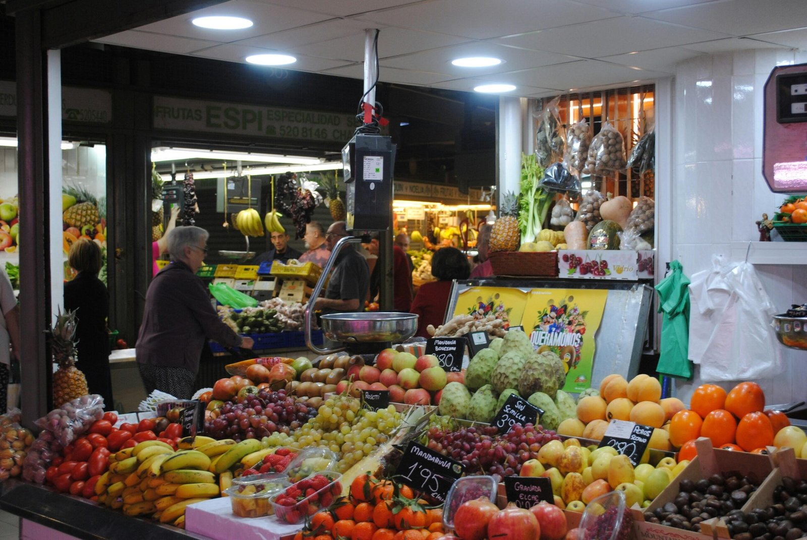Mann in grauer Jacke steht neben Obststand auf Mallorca, umgeben von frischen Früchten