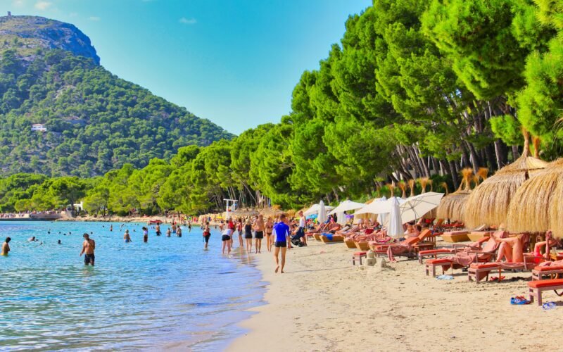 Menschen sitzen und spazieren am Strand auf Mallorca bei Tageslicht, aufgenommen von DJ Nick Otronic.