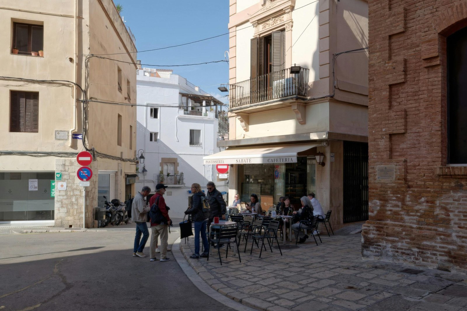 Menschen sitzen bei Sonnenschein an einem Straßencafé auf Mallorca, umgeben von einer belebten Straße