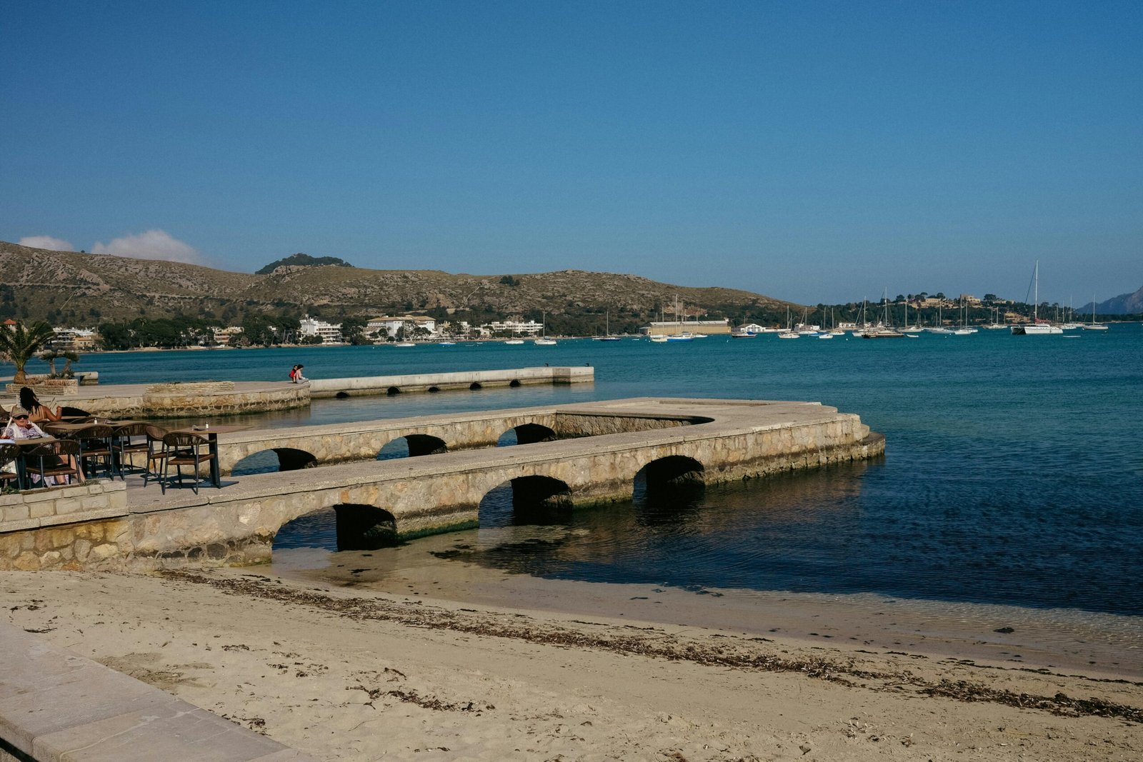 Menschen sitzen an Tischen auf einer Pier nahe dem Wasser auf Mallorca, aufgenommen von Konstantin Chemeris.