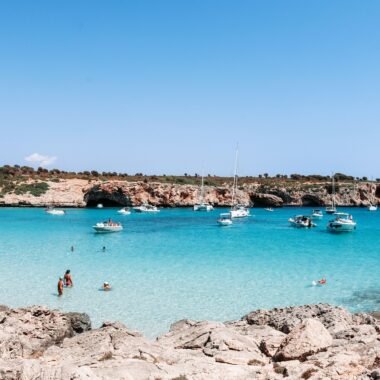 Menschen schwimmen im klaren Wasser auf Mallorca bei Tageslicht, während sie den Strand genießen, aufgenommen von Austin Farrington