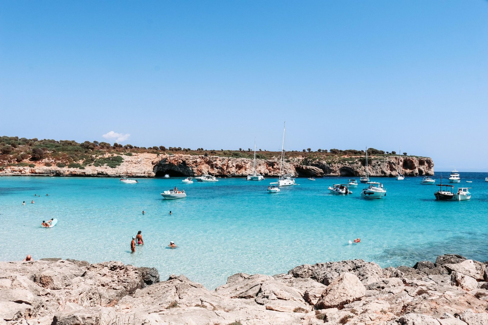 Menschen schwimmen im klaren Wasser auf Mallorca während des Tages, im Hintergrund der Strand und Himmel