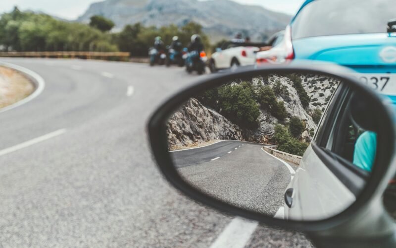 Schwarzer Autospiegel zeigt vorbeifahrende Autos auf Mallorca bei Tageslicht, aufgenommen von Eugene Zhyvchik.