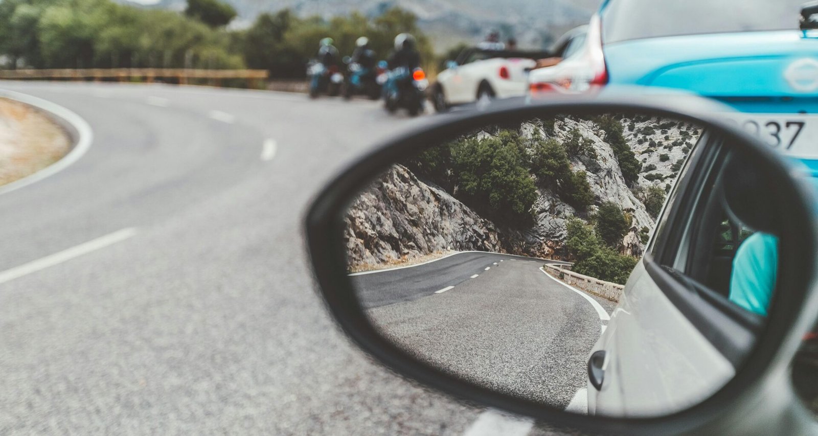 Schwarzer Autospiegel auf Mallorca zeigt vorbeifahrende Autos auf der Straße bei Tageslicht