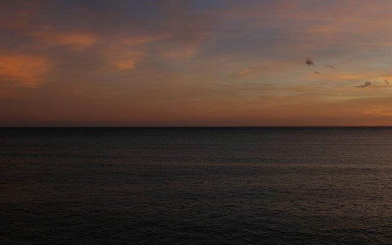 Sonnenuntergang über dem ruhigen Meer auf Mallorca, aufgenommen von Susana Bartolome, mit sanften Wellen und warmem Himmel.