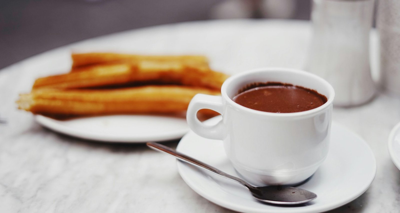 Tasse Schokoladendrink mit einer Platte Churros auf Mallorca, fotografiert von Oscar Nord.