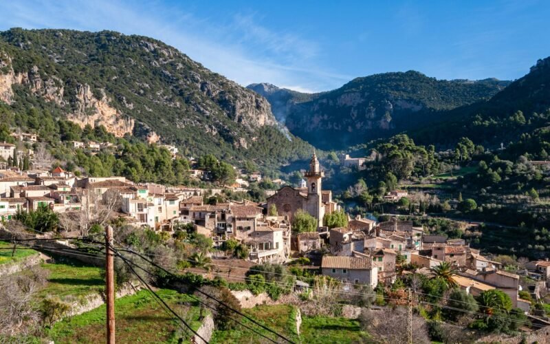 Weiße und braune Betonhäuser nahe grüner Berg unter blauem Himmel auf Mallorca, fotografiert von David Vives