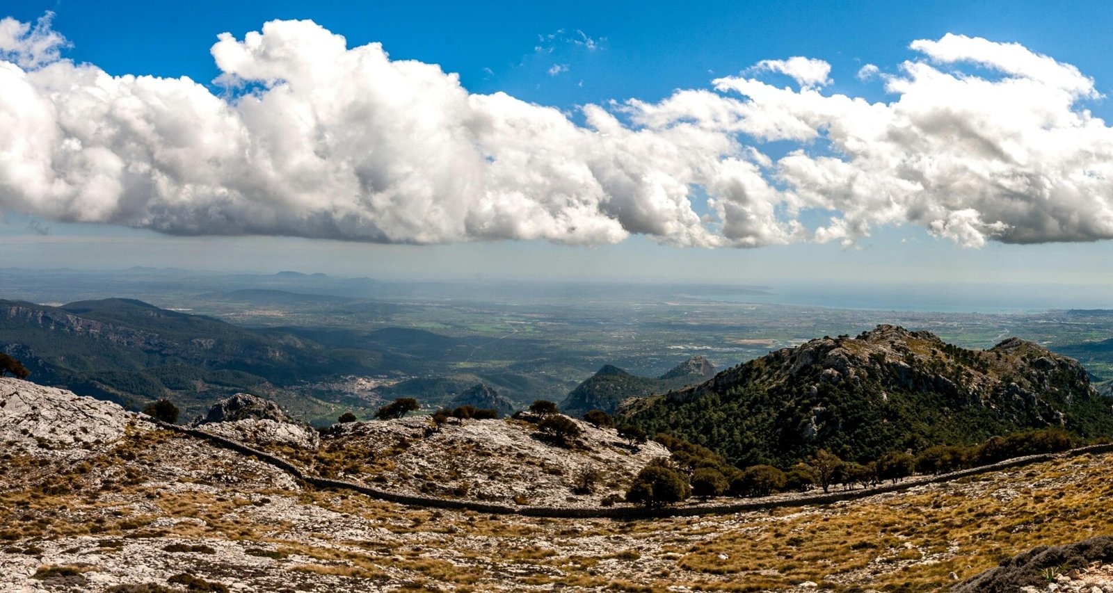 Weiße Wolken ziehen über die braunen Berge auf Mallorca, aufgenommen von David Vives.