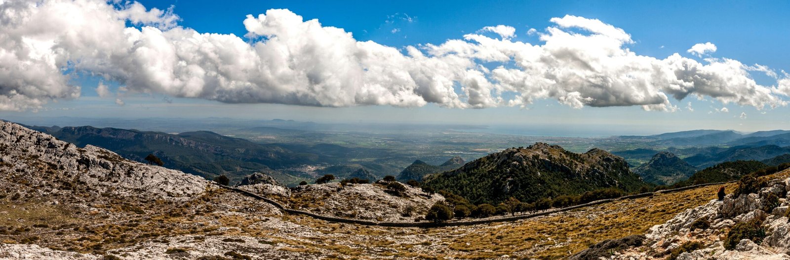 Weiße Wolken schweben über den braunen Bergen auf Mallorca, aufgenommen von David Vives.
