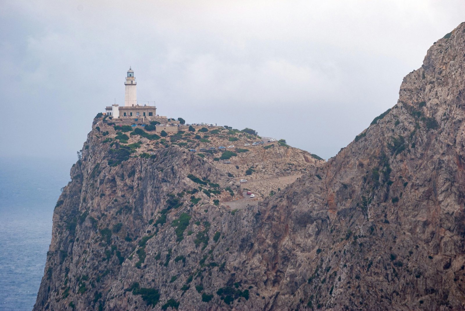 Weiße Betongebäude auf Mallorca vor felsiger Bergkulisse unter weißem Himmel bei Tageslicht