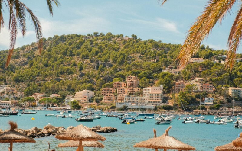 Boote in einer Bucht auf Mallorca, umgeben von Palmen und Gebäuden, aufgenommen von Alexis Presa.