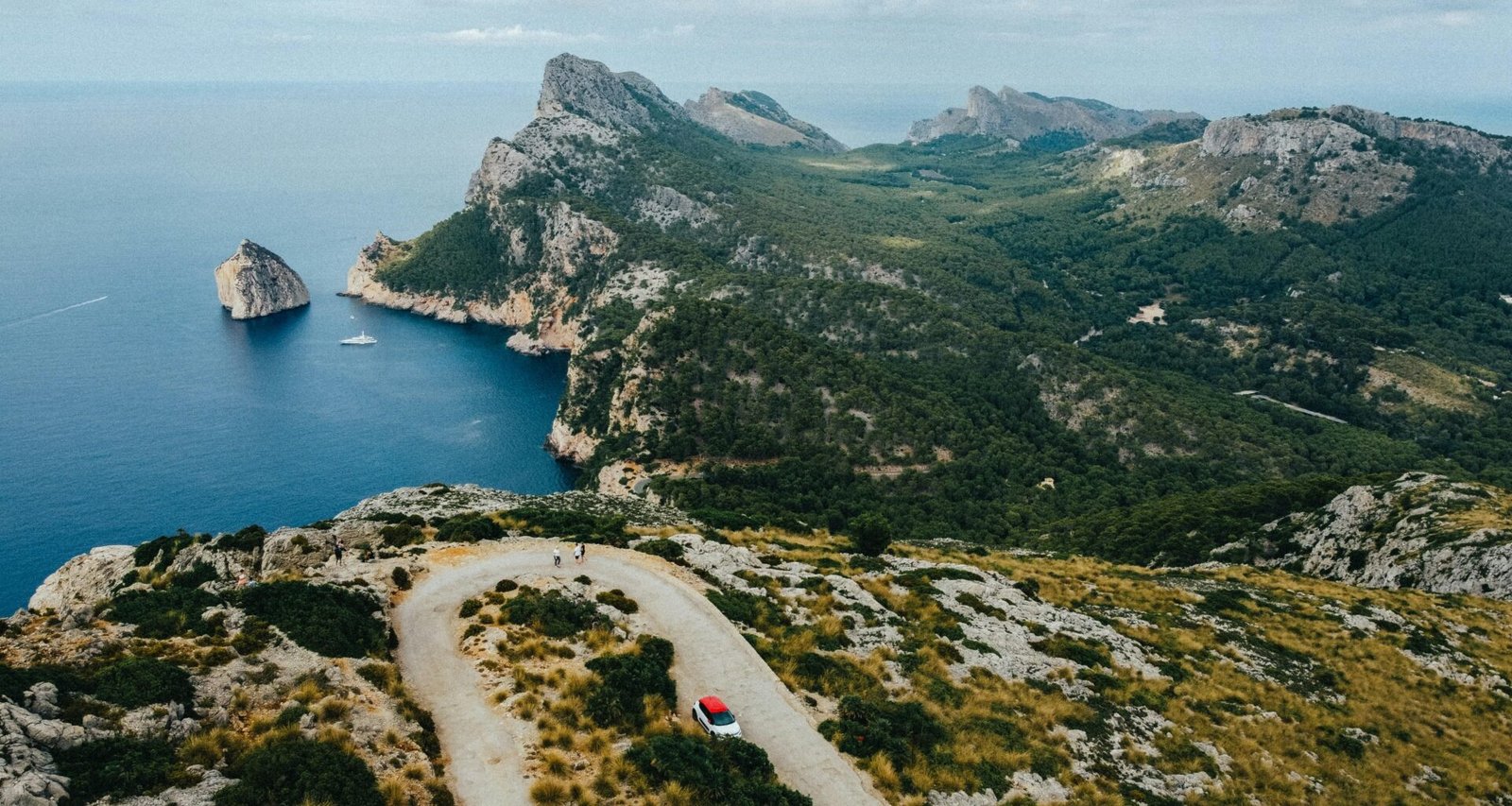 Ein Auto fährt auf Mallorca eine Straße entlang mit Bergen im Hintergrund, aufgenommen von Austin Farrington.