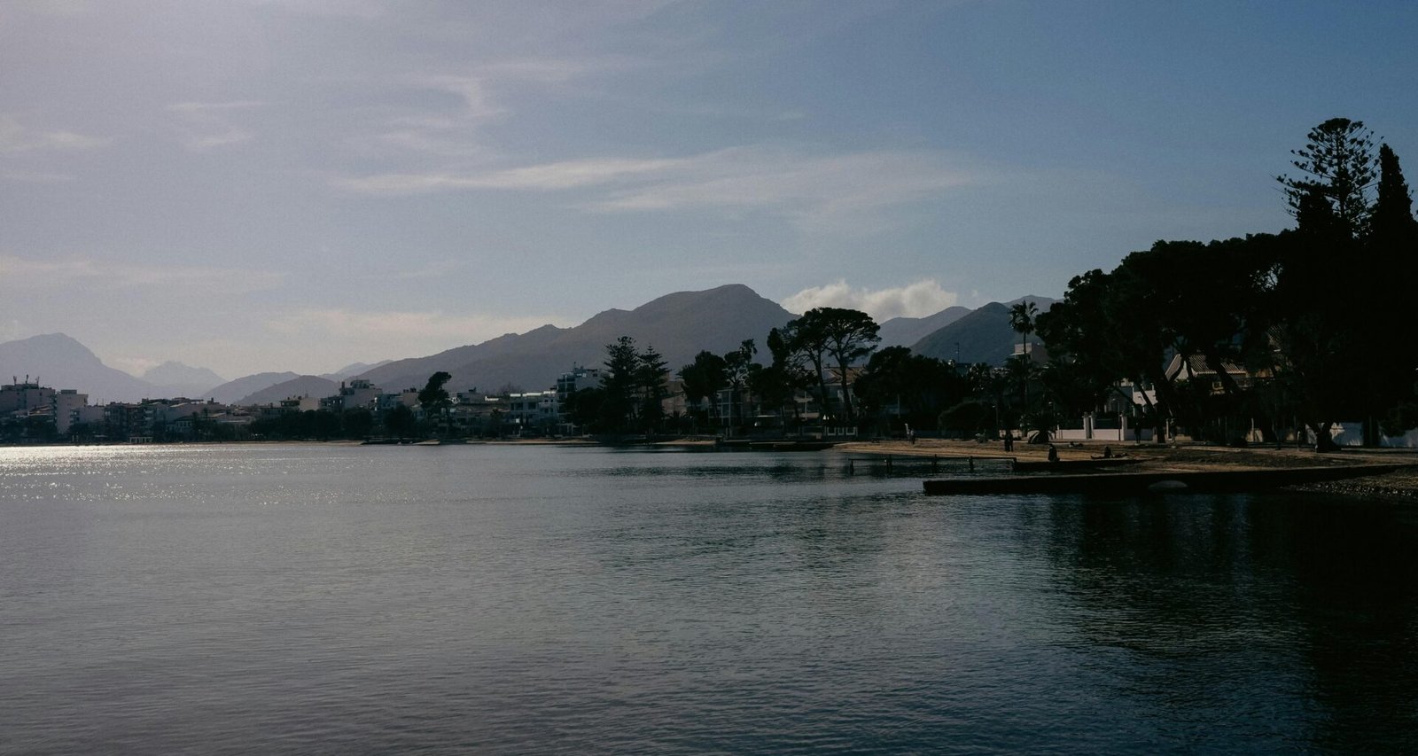 Ein ruhiger Wasserbereich auf Mallorca, umgeben von Bäumen und Bergen, aufgenommen von Konstantin Chemeris.