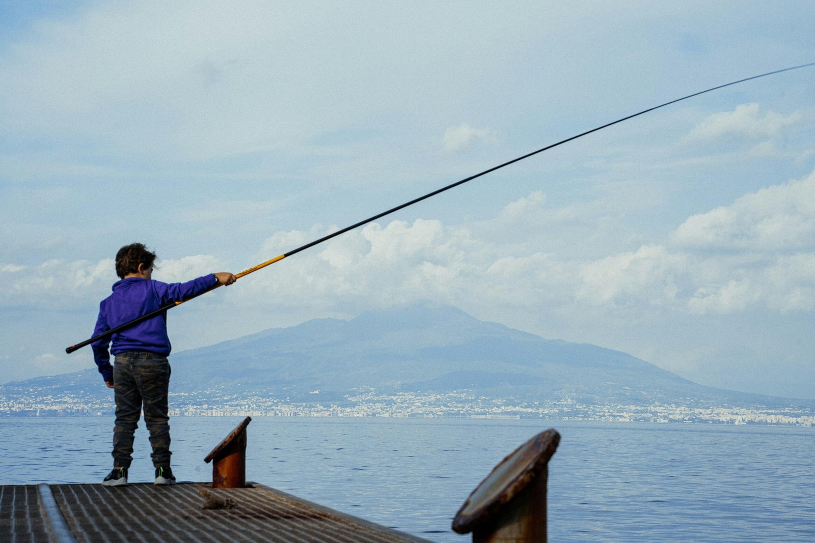 Mann steht auf Mallorca auf einem Dock und hält eine Angelrute, bereit zum Angeln im Hafen