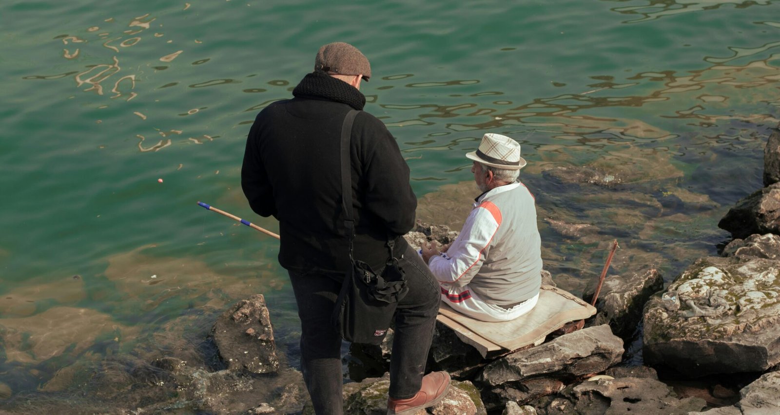 Ein Mann und eine Frau sitzen auf einem Felsen neben Wasser auf Mallorca, fotografiert von Sajad Emad.
