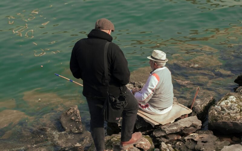 Ein Mann und eine Frau sitzen auf einem Felsen neben Wasser auf Mallorca, fotografiert von Sajad Emad.