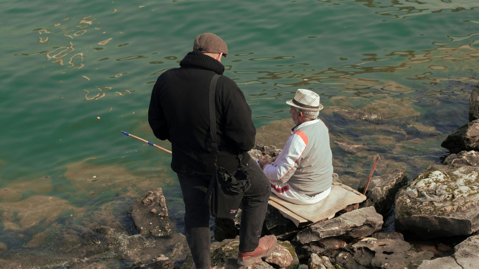 Ein Mann und eine Frau sitzen auf einem Felsen neben Wasser auf Mallorca, fotografiert von Sajad Emad.