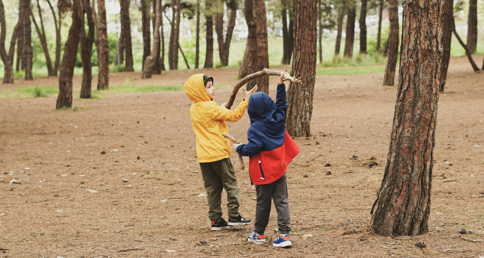 Zwei Kinder stehen nebeneinander im Wald auf Mallorca, umgeben von Bäumen und Natur, aufgenommen von Duygu Güngör.