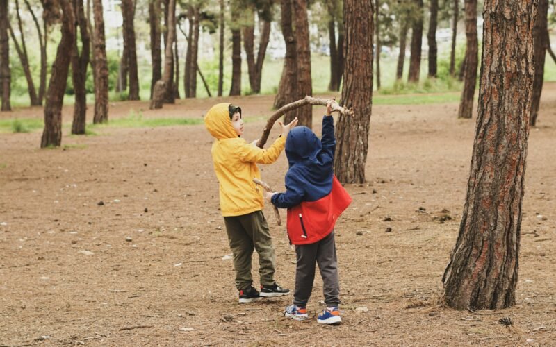 Zwei Kinder stehen nebeneinander im Wald auf Mallorca, umgeben von Bäumen und Natur, aufgenommen von Duygu Güngör.