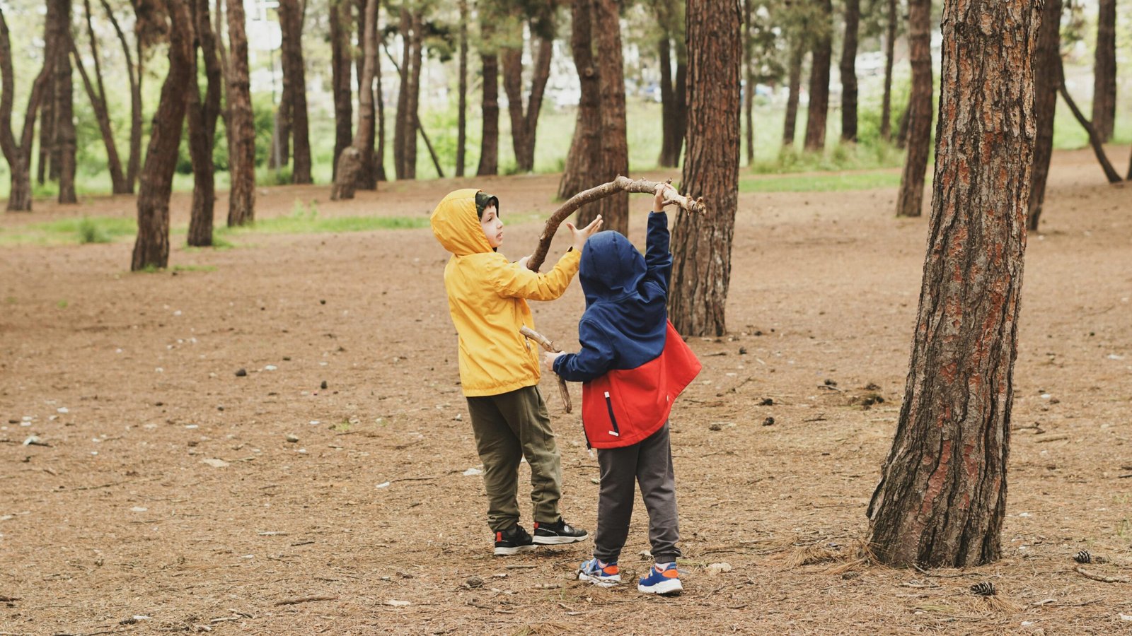 Zwei Kinder stehen nebeneinander im Wald auf Mallorca, umgeben von Bäumen und Natur, aufgenommen von Duygu Güngör.
