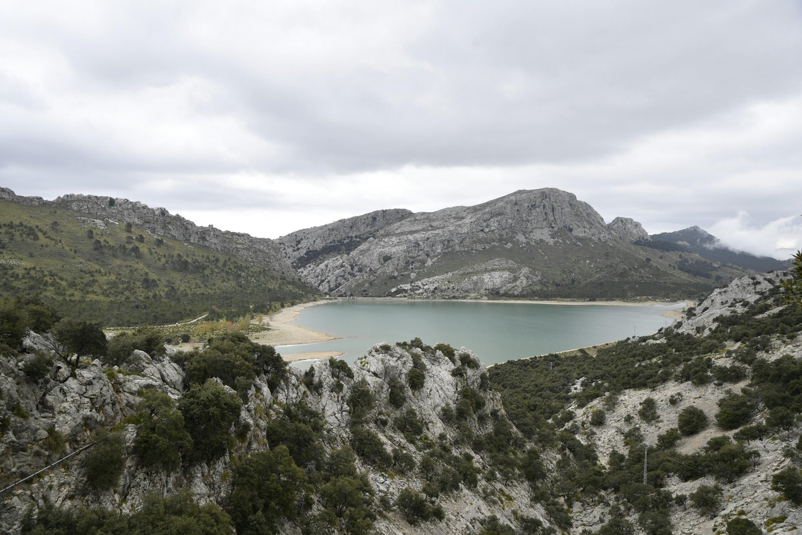 Serener See auf Mallorca mit felsigen, bewaldeten Hügeln im Hintergrund, aufgenommen von Margo Evardson.