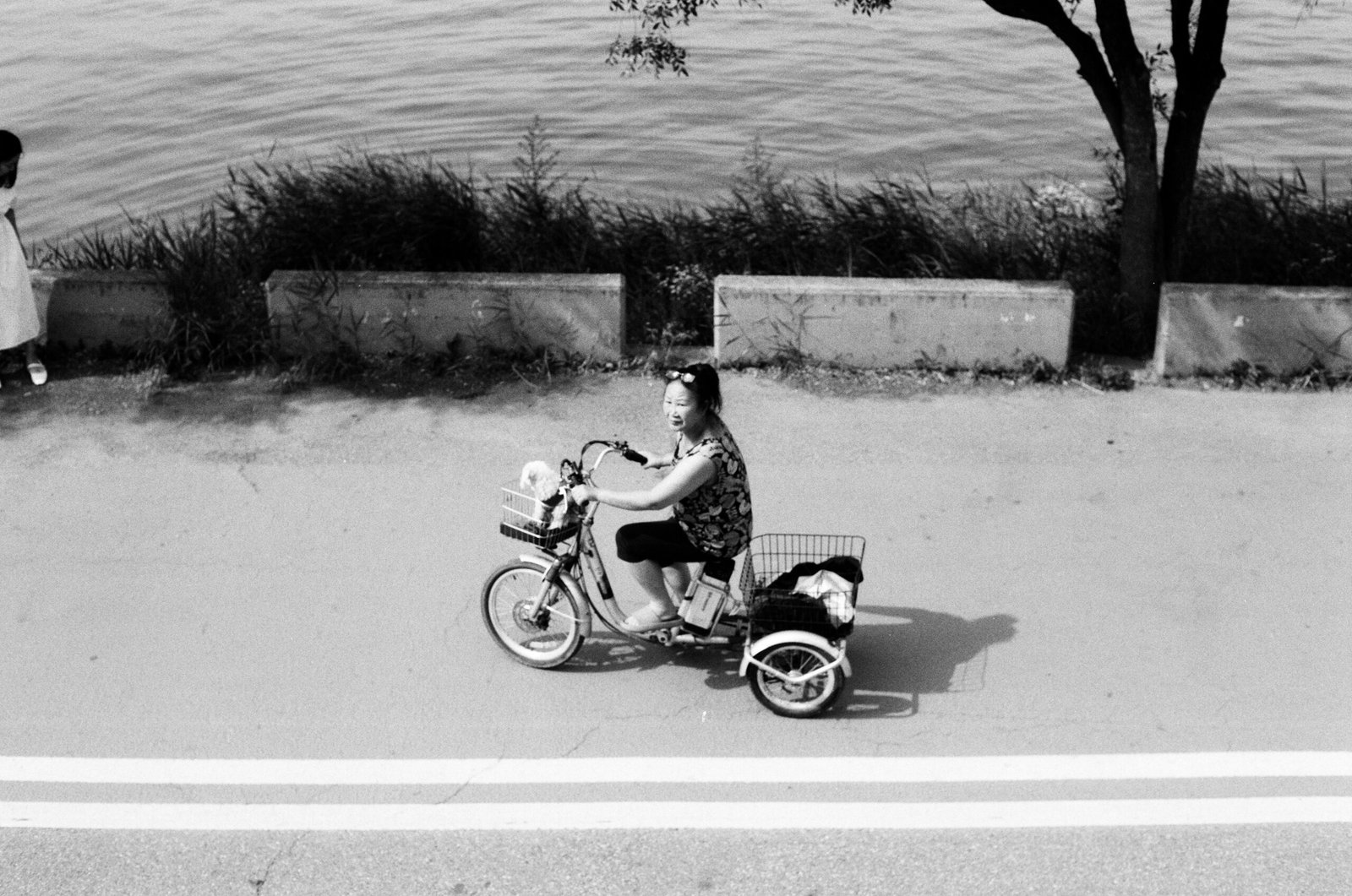 Frau fährt mit Fahrrad auf Mallorca, Baby im Korb sitzend, umgeben von mediterraner Landschaft, aufgenommen von Hoseung Han