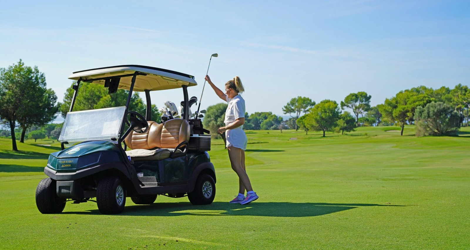 Frau steht neben einem Golfwagen auf einem Golfplatz auf Mallorca, fotografiert von Frederik Rosar.