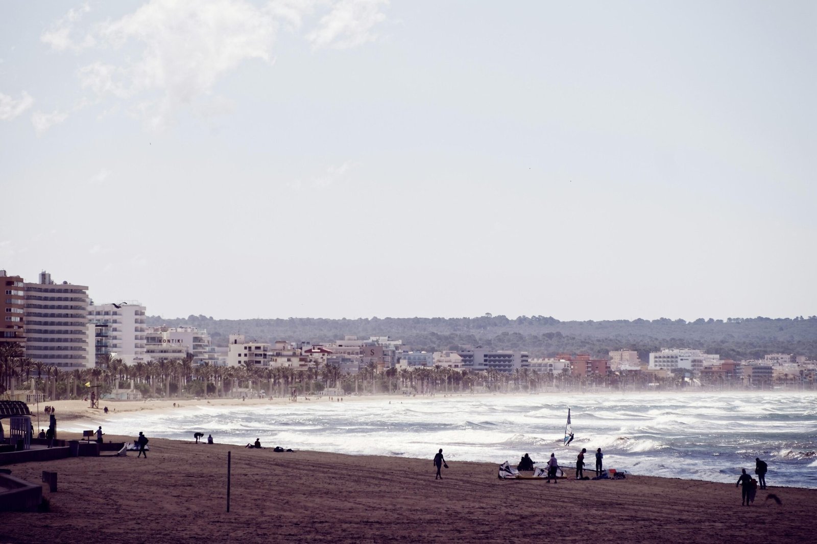Gruppe von Menschen steht auf einem Sandstrand auf Mallorca, Blick auf das Meer im Hintergrund