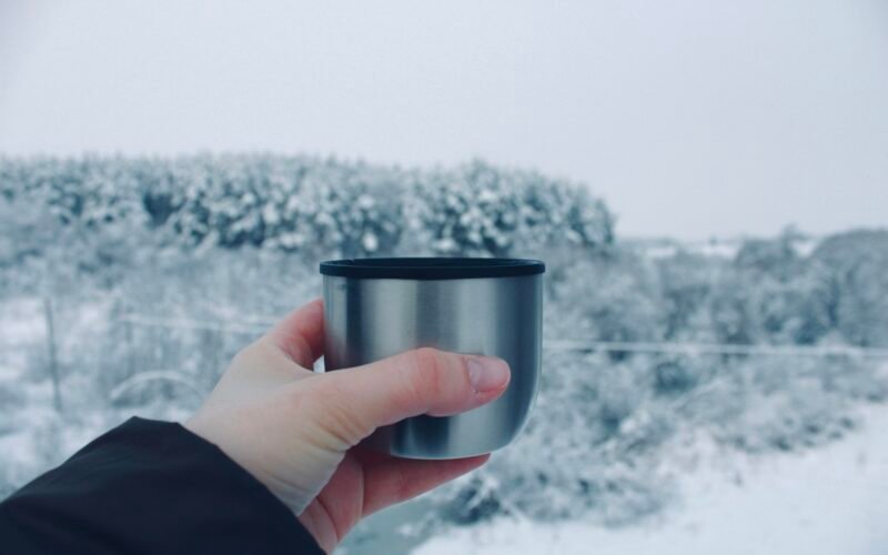 Person hält eine Tasse vor einer verschneiten Landschaft auf Mallorca, aufgenommen von Veronica Mihaylovskaya