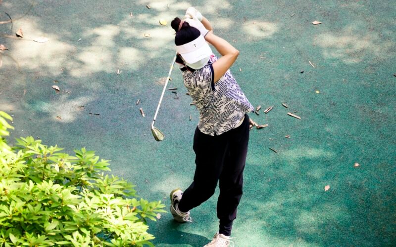 Person hält einen Golfschläger auf Mallorca, bereit zum Abschlag, mit grünem Golfplatz im Hintergrund