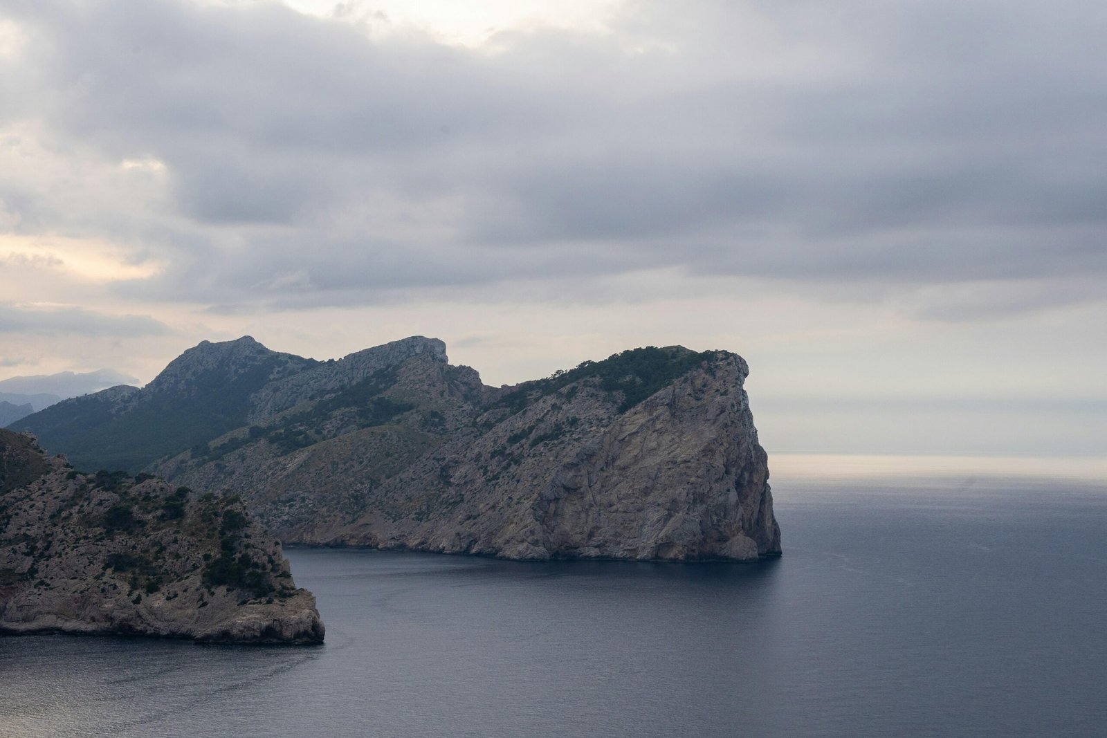 Felsige Küste auf Mallorca mit ruhigem Wasser und bewölktem Himmel, aufgenommen von Tim Bernhard