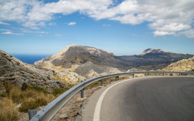 Graue Betonstraße führt vorbei an einem braunen Berg unter blauem Himmel auf Mallorca, aufgenommen von Milada Vigerova.