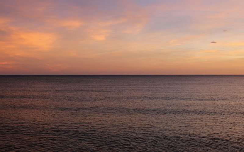 Das Meer auf Mallorca spiegelt den Sonnenuntergang wider, mit sanften Wellen und warmen Farben am Himmel.