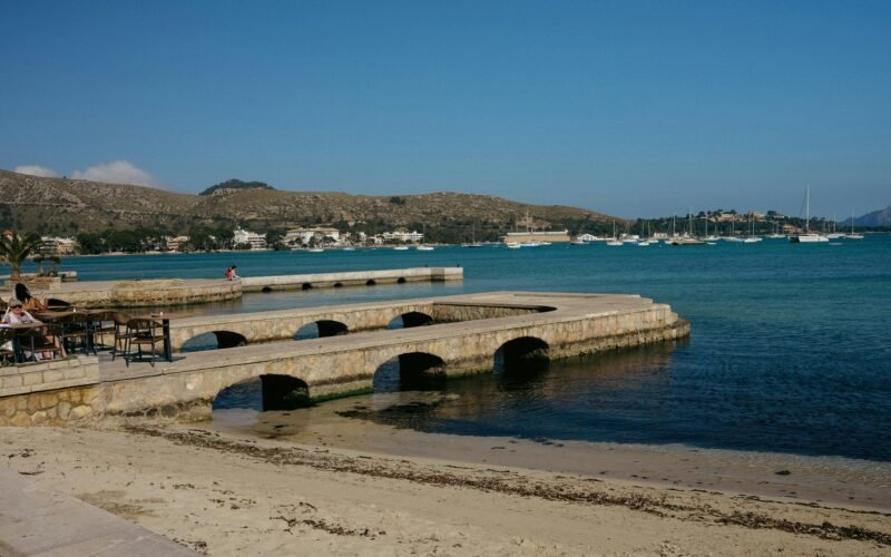 Menschen sitzen an einem Pier auf Mallorca am Wasser und genießen die Aussicht, aufgenommen von Konstantin Chemeris.