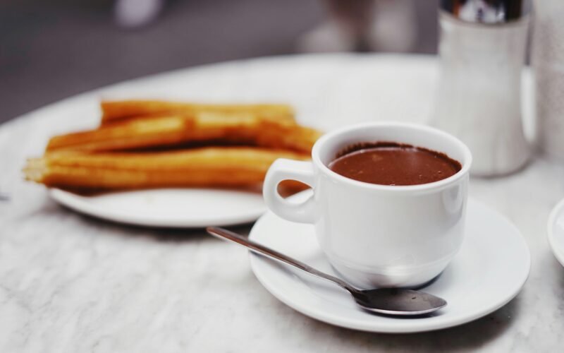 Tasse mit Schokoladendrink und eine Platte Churros auf Mallorca, fotografiert von Oscar Nord