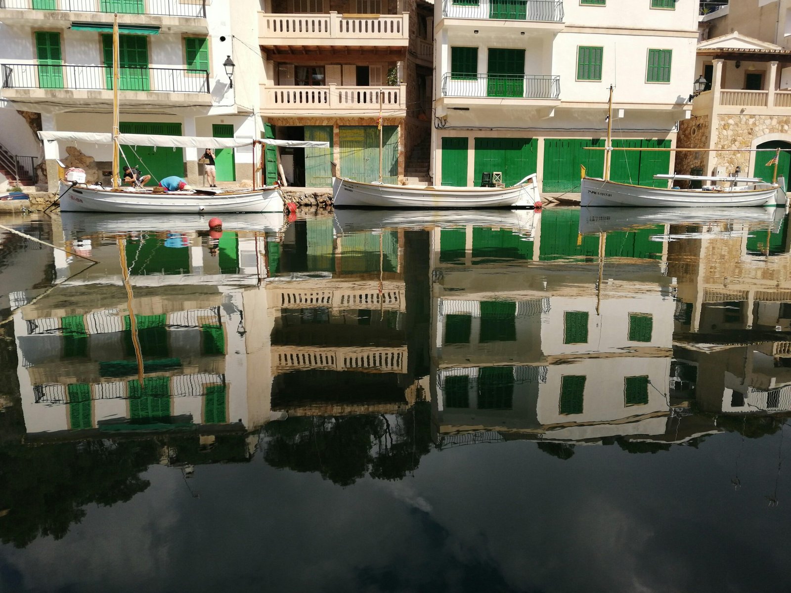 Weiße Boote liegen neben Gebäuden auf Mallorca auf dem Wasser, aufgenommen von Jacques Leideck.