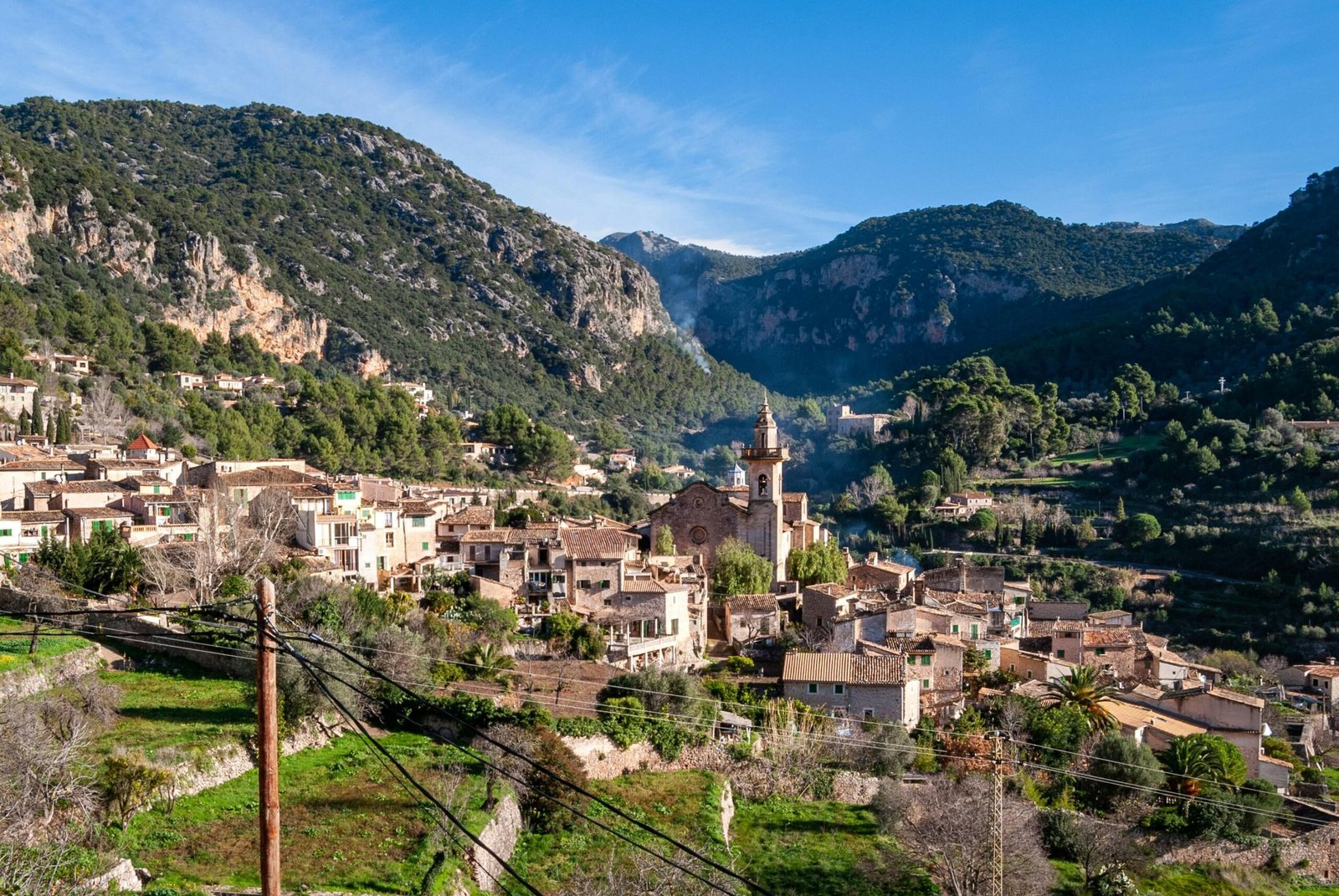 Weiße und braune Betone Häuser auf Mallorca neben grünen Bergen unter blauem Himmel bei Tageslicht, fotografiert von David Vives.